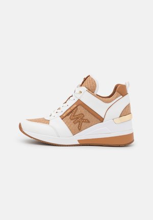 Baskets d'athlétisme blanches et beiges avec une tige texturée, des accents dorés, une semelle en coin et un laçage avec un logo sur le côté.