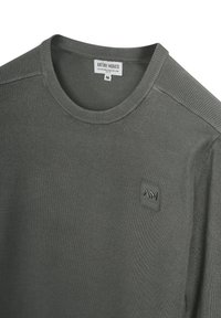 Maglione leggero di colore verde scuro con scollatura rotonda, dettagli a costine sulle spalle e una toppa con logo cucita sul petto.