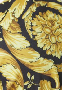 Černá látka se zlatým květinovým vzorem, který obsahuje velké listy a propracované květinové designy, hladkou strukturu a živý barevný kontrast.