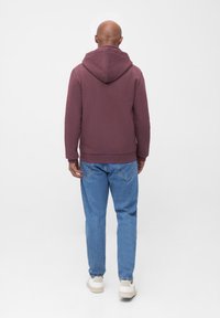 Kastanienbrauner Kapuzenpullover mit Kordelzug, langen Ärmeln und geripptem Saum, kombiniert mit hellblauen Jeans und weißen Sneakers.