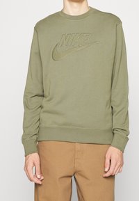 Sweatshirt Nike vert olive avec un logo texturé en grand format, doté d'un col rond et de poignets côtelés. Matière douce et décontractée.