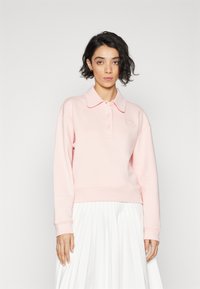 Sudadera de polo rosa claro con una textura suave, que presenta un cuello con solapa, tres botones y puños acanalados, combinado con una falda blanca con pliegues.