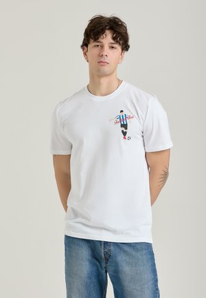 Hvid bomulds-T-shirt med et farverigt grafisk motiv af en fodboldspiller i færd med at sparke, med teksten "Football Fun" og blå, sort og rød accentuer.