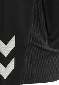 Primo piano di tessuto nero con pannello strutturato e due strisce bianche a chevron con sottili linee ondulate su materiale liscio.