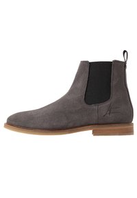 Stivale Chelsea in suede grigio con pannelli elasticizzati ai lati, punta tondeggiante e suola di un marrone chiaro a contrasto. Presenta un linguetta di pull sul retro.