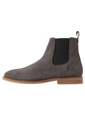 Grey suede Chelsea boot with elastic side panels, rounded toe, and a contrasting light brown sole. Features a pull tab at the rear.