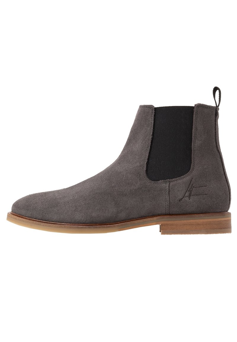 Stivale Chelsea in suede grigio con pannelli elasticizzati ai lati, punta tondeggiante e suola di un marrone chiaro a contrasto. Presenta un linguetta di pull sul retro.