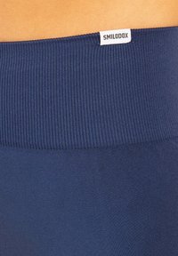 Námořnické modré legíny s ribbovaným pasem, s bílou etiketou nahoře. Textura je hladká a elastická.