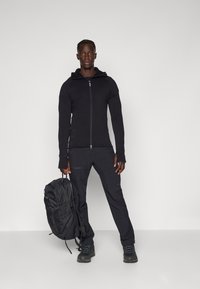 Black zip-up hoodie, black athletic pants, and black backpack. Smooth fabric, fitted design, and sturdy hardware. Standing position with shoes.