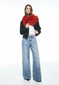 Sciarpa rossa e soffice avvolta intorno al collo, abbinata a una giacca corta nera e un top corto bianco. Jeans larghi a gamba larga azzurri completano il look.