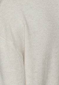 Pull en maille de couleur crème, présentant une texture douce, une coupe décontractée et des détails côtelés subtils au niveau de l'encolure et de l'ourlet.