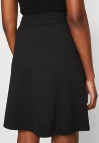 Jupe patineuse noire avec une taille élastique texturée et un tissu lisse. Forme simple en A avec un ourlet qui se courbe doucement.