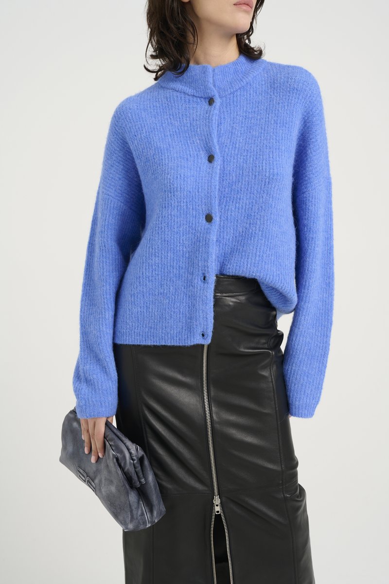 Hellblau gestrickte Cardigan mit hohem Kragen und schwarzen Knöpfen, kombiniert mit einem schwarzen Lederrock mit Reißverschluss vorne. Strukturiertes Material.