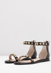 Sandali pianeggianti neri con decorazioni in tono oro sulle cinghie, design open toe e una soletta dal texture liscia.