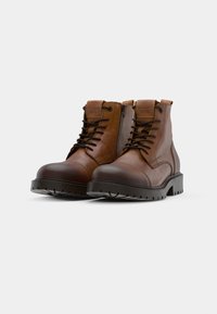 Botas de tobillo de cuero marrón con punta redondeada, diseño con cordones, cremallera lateral, suela texturada y suela de goma oscura en contraste.
