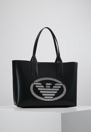 Schwarze Ledertasche mit zwei Griffen und einem großen ovalen Emblem auf der Vorderseite, das einen stilisierten Adler aus kleinen weißen Nieten zeigt.