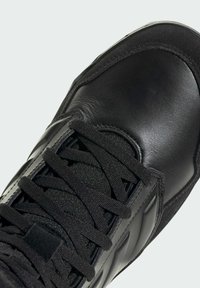 Black athletic shoe with synthetic leather and textured upper, featuring flat laces, a padded collar, and smooth toe cap.
