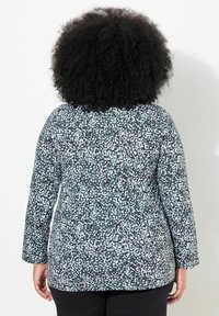 Langärmliges Oberteil mit einem schwarz-weißen gesprenkelten Muster, enganliegendem Design und abgerundetem Saum, aus einem weichen, dehnbaren Stoff gefertigt.