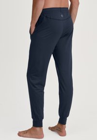 Marineblauwe joggingsbroeken gemaakt van een gladde stof, met een elastische tailleband, zijzakken en taps toelopende boorden bij de enkels.