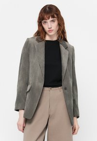 Gray corduroy blazer with a notched lapel, single button closure, and front pockets, paired with a black top and beige trousers.