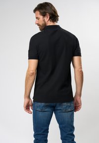 Black polo shirt with collar, short sleeves, and a straight cut, paired with blue denim jeans, featuring a faded wash and back pockets.