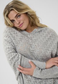 Grau gestrickter Pullover mit einem geometrischen Spitzendesign, lockerer Schnitt und gerippten Bündchen. Texturierte Oberfläche und lässige Passform.