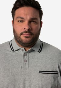 Šedé polo tričko s tříknoflíkovou légou, náprsní kapsou a kontrastním černým pruhovaným límcem a lemováním kapsy. Hladká struktura látky.