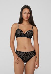 Conjunto de lencería negra que incluye un sujetador de encaje floral transparente con copas con aros y tirantes ajustables, combinado con bragas de encaje a juego.