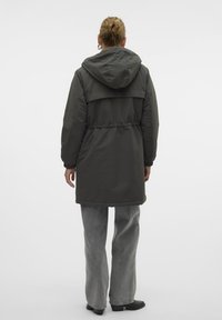 Długa, ciemnoszara kurtka puchowa z kapturem, elastycznym pasem i luźnym krojem. Do tego jasnoszare szerokie spodnie i czarne botki za kostkę.