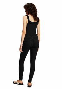 Top negro de tirantes acanalado con volantes, combinado con jeans skinny negros y sandalias planas con tiras blancas.
