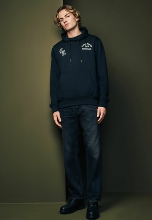 Black hoodie with front pocket, white graphic details. Paired with dark denim jeans and black boots. Simple, casual design.