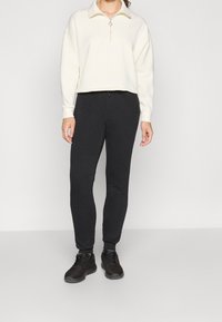 Krémový svetr s půlzipem na límci, spojený s černými úzkými tepláky a černými sportovními botami. Měkká látka, minimalistický design, bez vzorů.