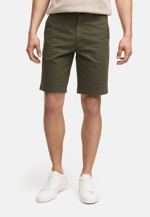 Olivenfarvede shorts lavet af bomuld, med lige pasform, forlommer og omviklede kanter, parret med hvide sneakers.