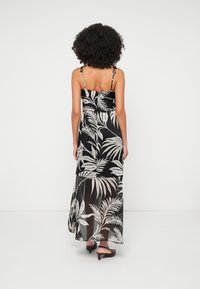 Maxiklänning i svart med ett tropiskt mönster av vita blad. Har tunna justerbara axelremmar och en genomskinlig nederkant. Slät tygtextur.