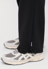 Black sweatpants with a straight cut and a small tag, paired with light gray athletic shoes featuring mesh panels and a cushioned sole.