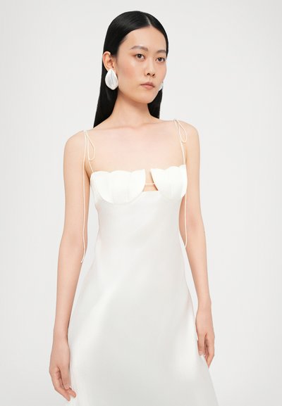 Rochie albă din satin cu un decolteu structurat și ondulat. Bretele subțiri și un design neted, fluid. Modelul poartă cercei mari albii, de efect.