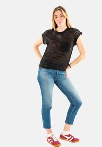 Haut noir en tricot à manches courtes avec une poche avant, associé à un jean skinny bleu clair et des baskets rouges et blanches avec une semelle en caoutchouc.