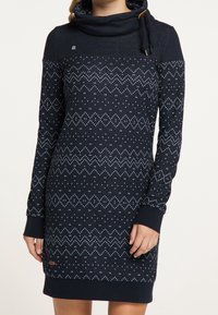 Meriai sininen neulemekko, jossa on kauluksellinen kaulus, geometrisiä vaaleansinisiä kuvioita, pitkät hihat ja kontrastoivat hihansuut. Rinnassa on pieni logo-yskä.