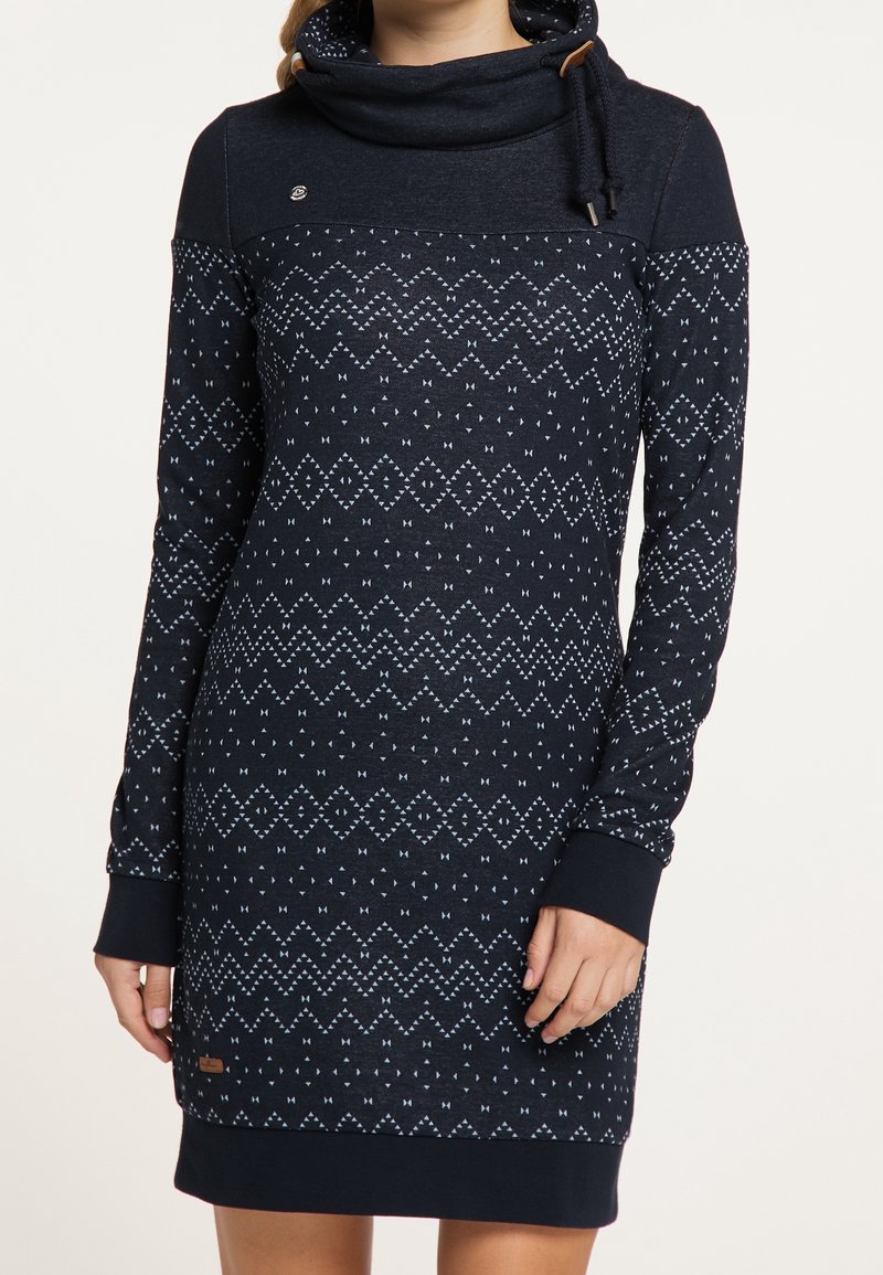 Meriai sininen neulemekko, jossa on kauluksellinen kaulus, geometrisiä vaaleansinisiä kuvioita, pitkät hihat ja kontrastoivat hihansuut. Rinnassa on pieni logo-yskä.