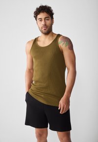 Olivgrünes geripptes Tanktop mit Rundhalsausschnitt, kombiniert mit schwarzen Shorts. Das Tanktop hat einen taillierten Schnitt und eine glatte Textur.