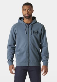 Sudadera con cremallera en tejido azul apagado con un bolsillo frontal, capucha ajustable y logo impreso en el pecho. Presenta puños y dobladillo de canalé.