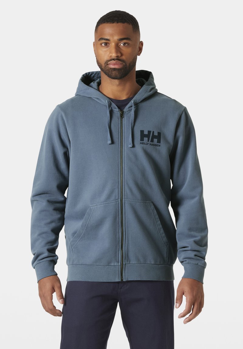 Sudadera con cremallera en tejido azul apagado con un bolsillo frontal, capucha ajustable y logo impreso en el pecho. Presenta puños y dobladillo de canalé.