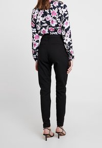 Pantalons noirs ajustés à taille haute, avec une texture lisse et une coupe slim, accompagnés d'un chemisier à motifs floraux avec des fleurs roses et blanches.