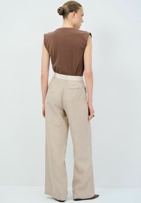 Bruine mouwloze top gecombineerd met hooggesneden, licht beige wijde broek, met een gestructureerde afwerking en een aansluitende tailleband.