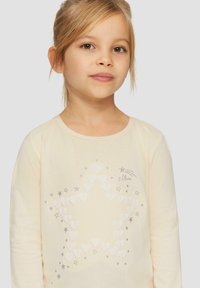 Langarm-Cremeshirt mit einem Sternenmotiv aus weißen Herzen und silbernen Sternen, mit leichter Textur und rundem Ausschnitt.