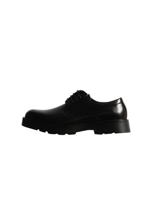 Chaussure noire en cuir à lacets, à bout arrondi et à semelle épaisse et rainurée, présentée de profil sur fond blanc.