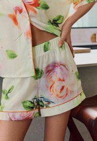 Loungewear set met bloemmotief in lichte stof. Top heeft een oranje rand; shorts hebben een elastische tailleband en elegante rozenontwerpen.