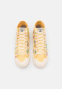 Höga sneakers i ljusgul canvas med färgglada broderade mönster, vita snören och gummidetaljer vid tån.