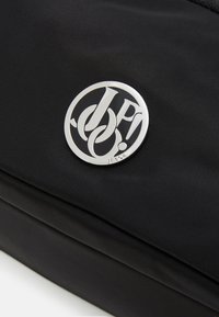 Zaino in tessuto nero con logo in metallo argentato, superficie texture con leggere riflessi, e chiusure lampo lisce.
