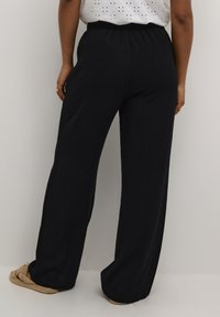 Zwarte, wijde broek met een elastische tailleband, gemaakt van een zachte stof. Gladde textuur en volledige lengte, geschikt voor casual draag.
